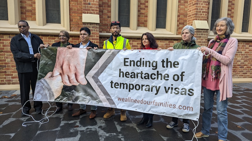 A group of people standing outside holding a banner that says "Ending the heartache of temporary visas".