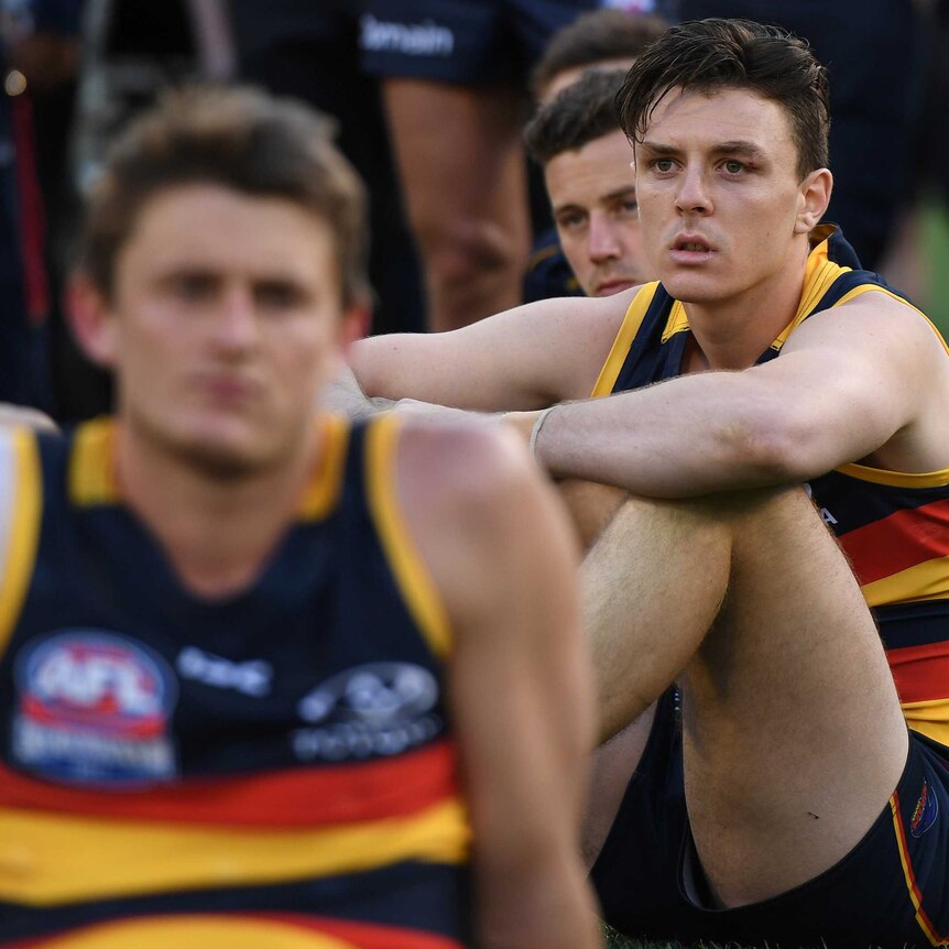 Crows player Jake Lever sits on the ground looking sad.