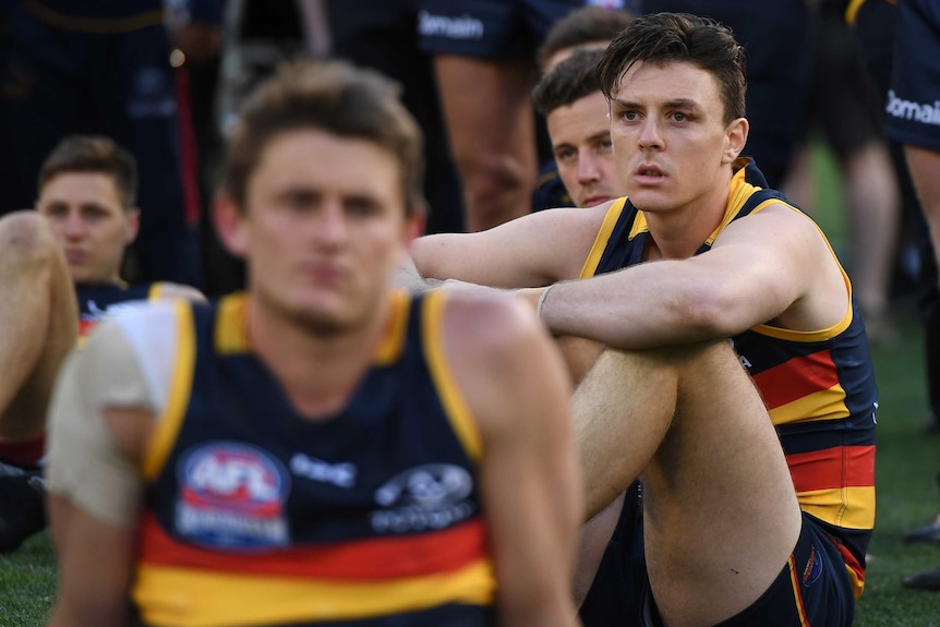 Crows player Jake Lever sits on the ground looking sad.