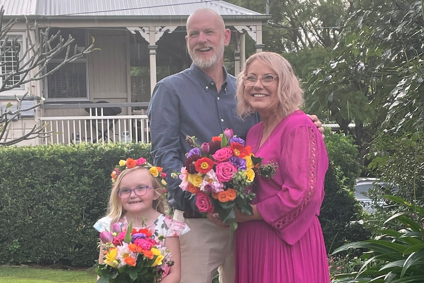 A couple and a young girl standing with flowers. 