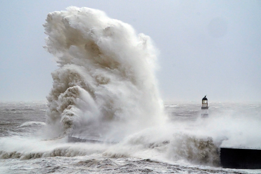 A huge wave crashes next to a lighthouse
