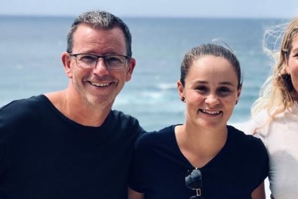 A man and a woman, both wearing black shirts, pose for a photo together near a beach.