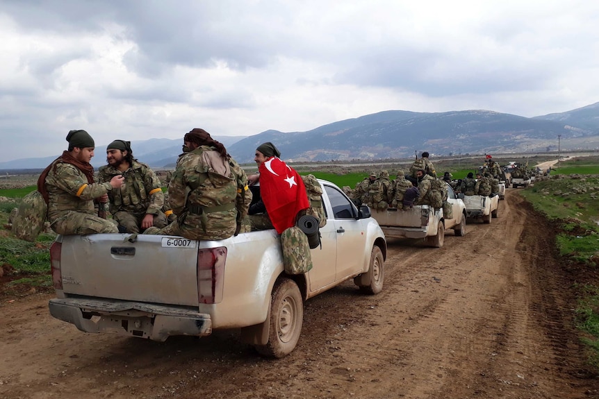 A line of trucks carrying soldiers moves down a dirt road.