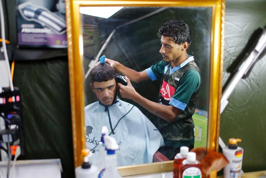 An Iraqi youth gets a haircut at an Erbil refugee camp