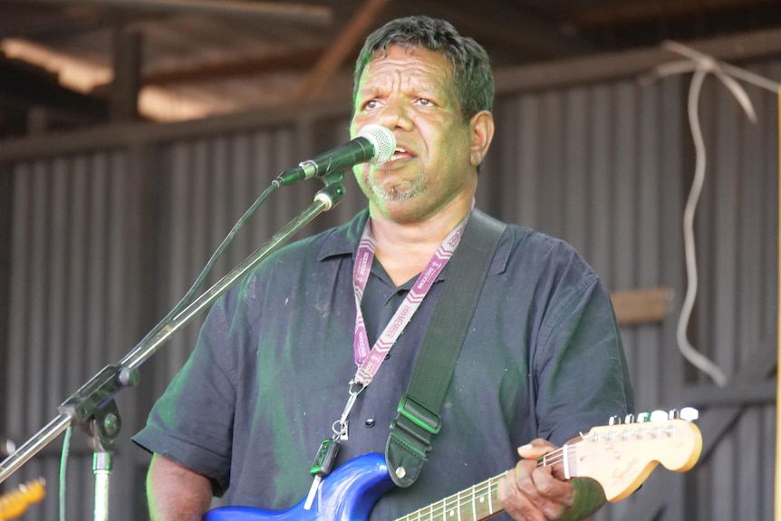 a man sings into a microphone while playing guitar