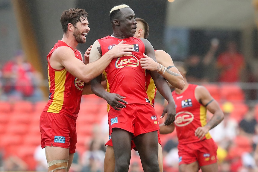 Three Gold Coast Suns AFL player embrace as they celebrate a goal against Fremantle.