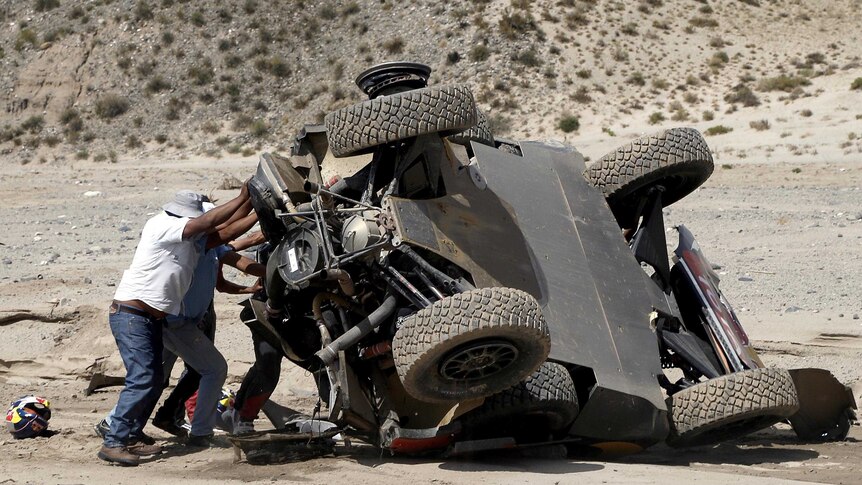 Spectators help Sebastien Loeb overturn his car in a desert landscape.
