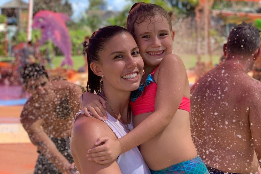 A woman hugs her daughter at a colourful waterpark.