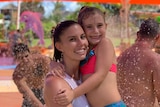 A woman hugs her daughter at a colourful waterpark.