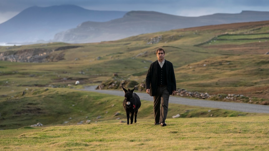 A troubled-looking middle-aged man in 20s-style dress walks through an Irish field, accompanied by a donkey