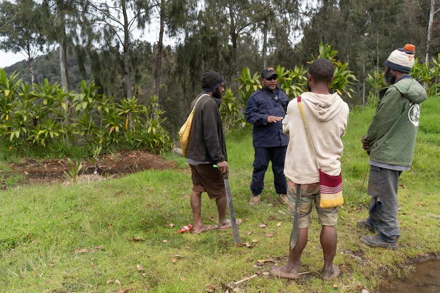 Police officer speaking to three PNG locals in a field next to a makeshift grave. 