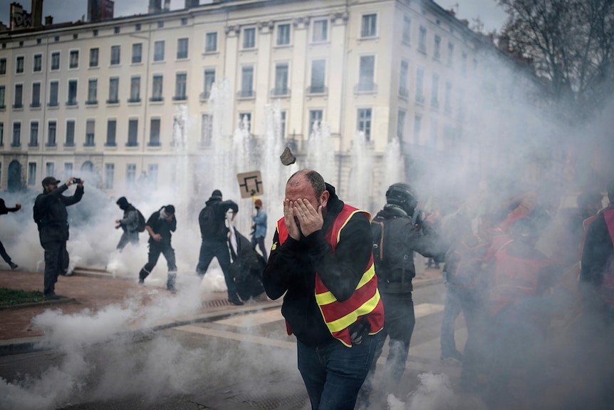 a protester covers his face as tear gas is fired on the streets of Lyon