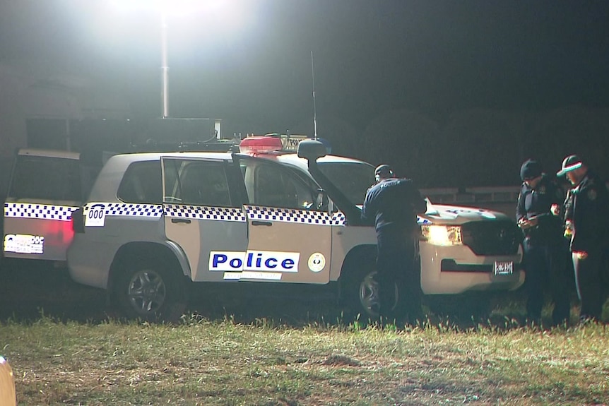 Police officers stand next to a police vehicle in a paddock, one is leaning on the bonnet writing on paper