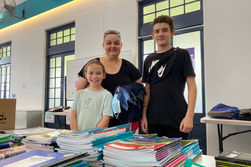 A woman with a boy and girl. They are standing in front of school books