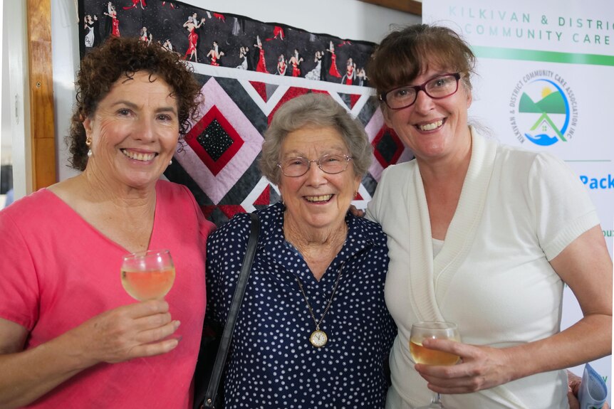 Three ladies smile at camera holding glasses of wine