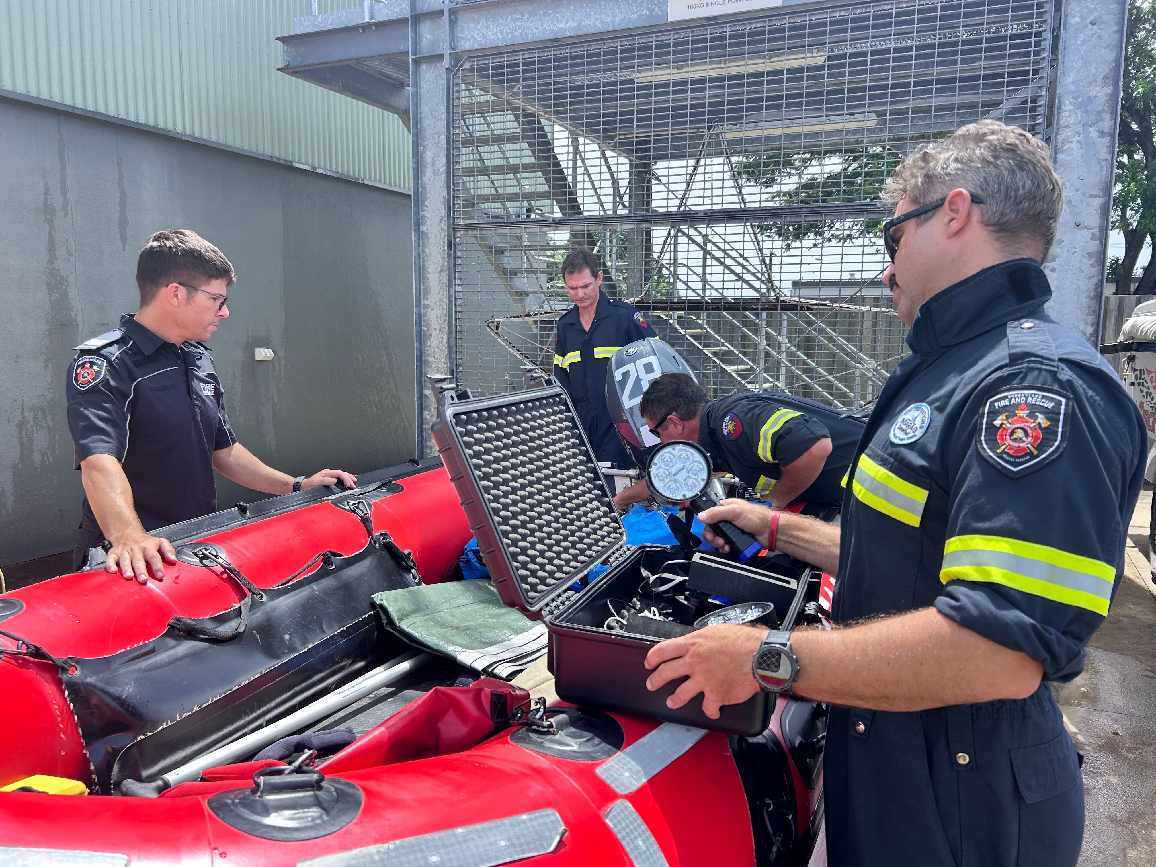 Hombres con uniformes del QFD se paran frente a un bote de rescate en aguas rápidas
