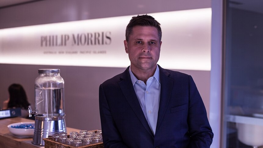 Patrick Muttart leans on a bar in front of Philip Morris corporate branding