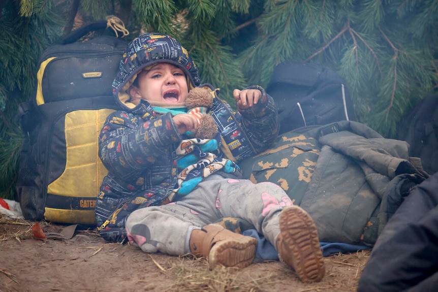 A child cries on the ground as other migrants from the Middle East and elsewhere gather at the Belarus-Poland border.