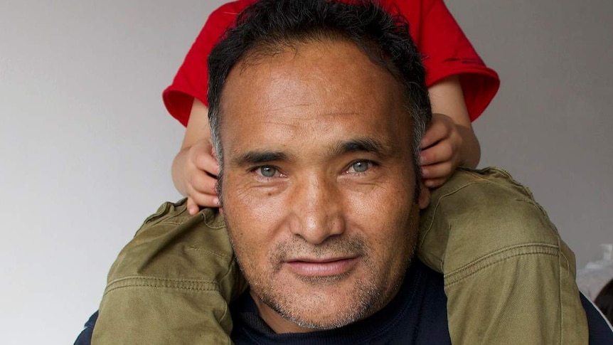 a man smiles at the camera with his son on his shoulders.