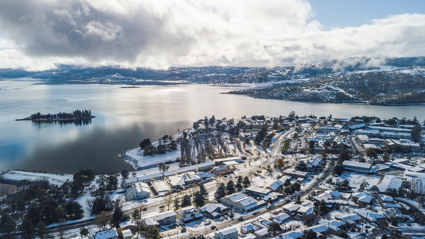 A drone shot of a town by a lake with snow.