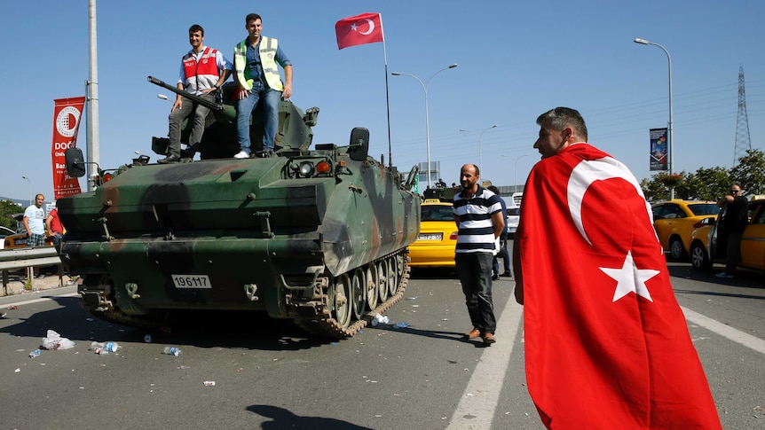 A man wrapped in a Turkish flag walks past a military vehicle in Istanbul.