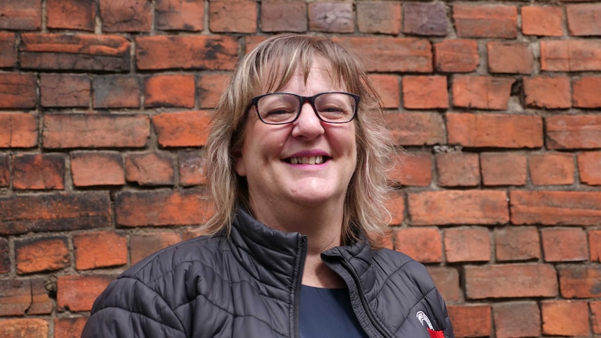 woman with glasses smiling at camera in front of brick wall