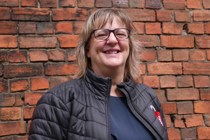 woman with glasses smiling at camera in front of brick wall