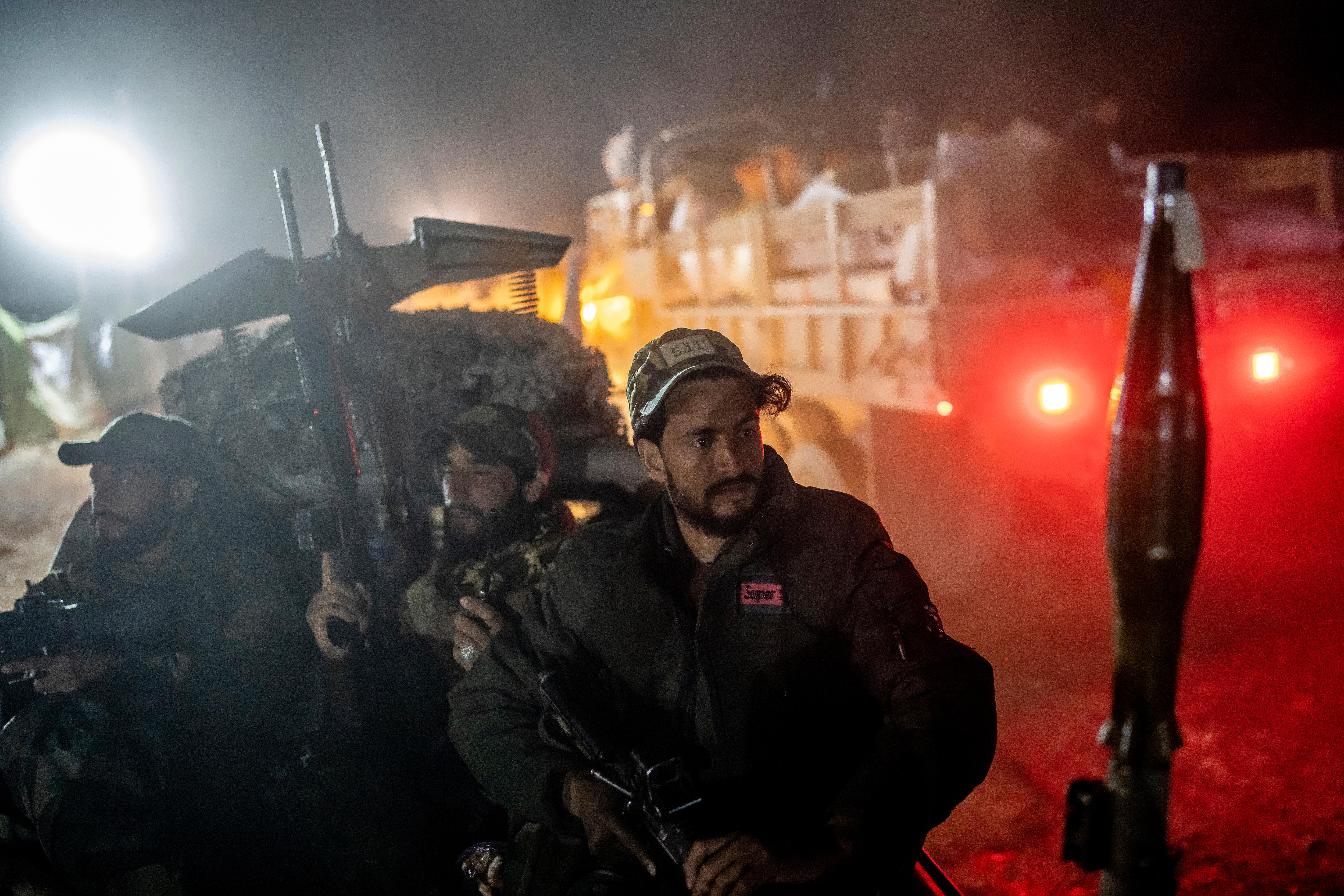 A group of men with gun stand near a truck in a darkened urban area