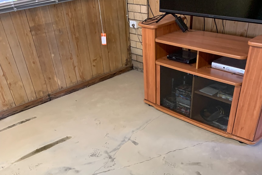 A layer of light grey silt surrounding a chipboard TV cabinet on a concrete floor