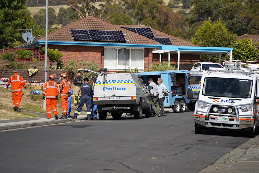 Several SES, police and Tasmania Fire Service officers stand around a police vehicle on a suburban street