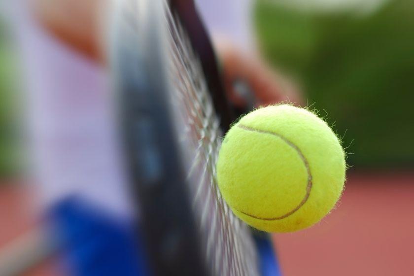 A tennis racket hits a green ball.
