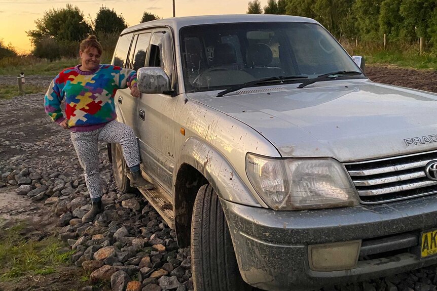 Sarah Riley-Smith is wearing a colourful jumper and pants and standing next to a 4WD.