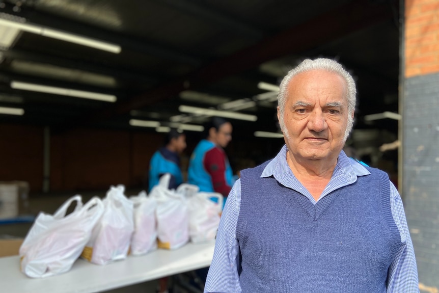 A man wearing a blue vest stands in front of a table holding plastic bags