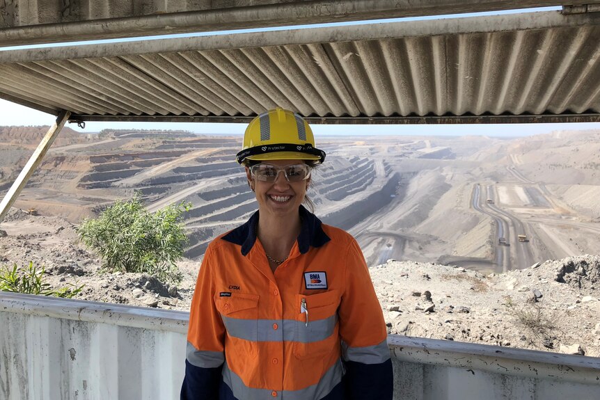 Mining manager in safety gear stands in front of huge dug out mine