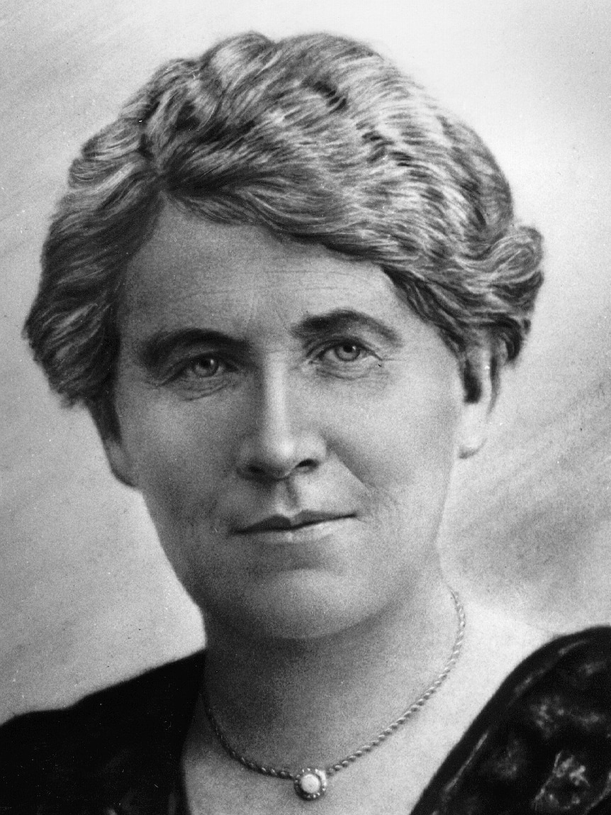 A black and white picture of a woman in the early 1900s wearing a black dress and necklace.