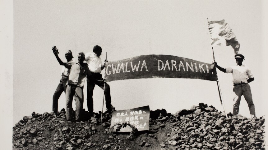 A photo showing a groupm of men holding a sign on top of a hill