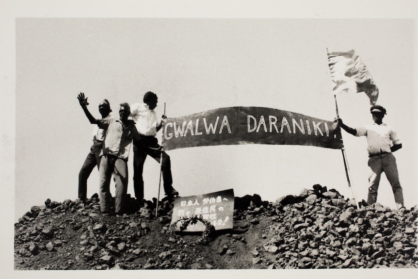 A historic photo of a group of Indigenous people holding a banner atop an iron stack.