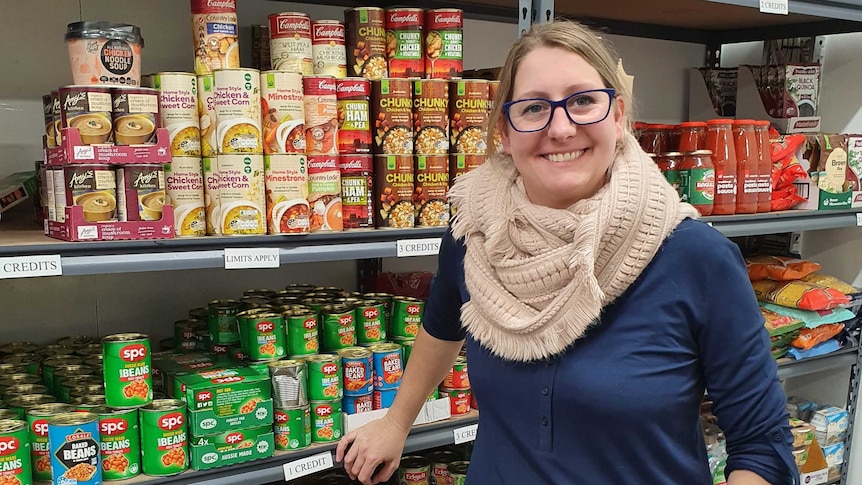 A lady stands in front of a shelf of tinned food