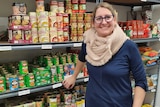 A lady stands in front of a shelf of tinned food