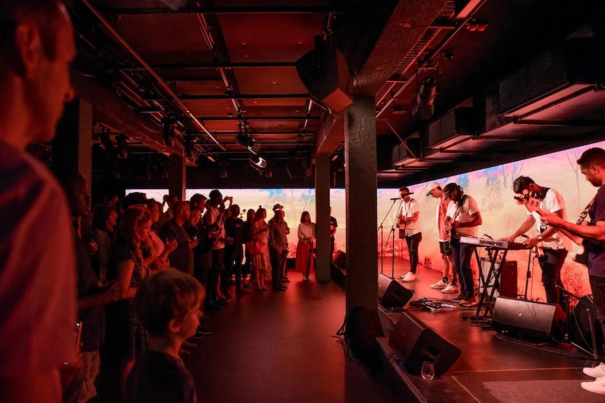 A band performs before a crowd with a long LED wall behind them.