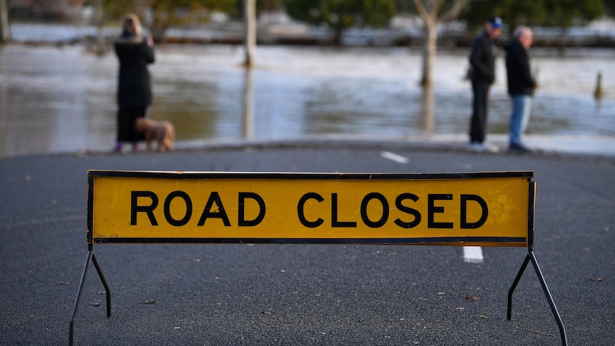 A road closed sign sits in the middle of a street in front of floodwaters