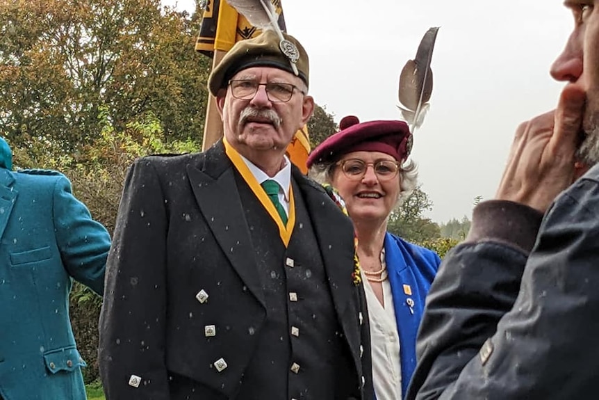 Paul and Shona stand in traditional Scottish attire featuring a black coat, maroon hat, green tie and blue jacket.