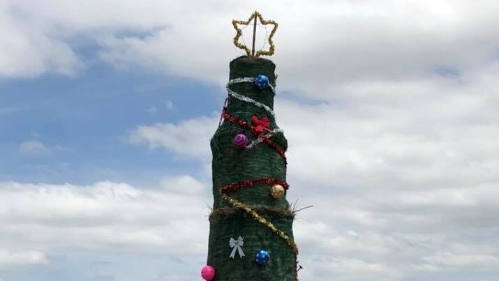 Hay bales piled up in field, painted green and wrapped in tinsel and baubles.