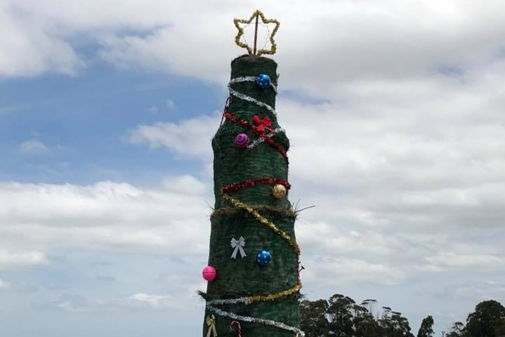 Hay bales piled up in field, painted green and wrapped in tinsel and baubles.