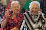 Two elderly Indonesian women smiling while sitting next to each other.