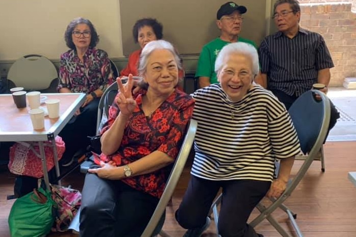 Two elderly Indonesian women smiling while sitting next to each other.