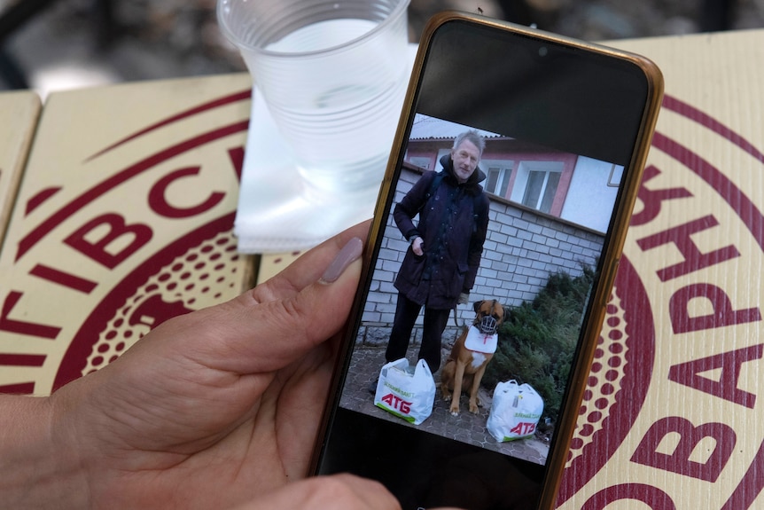Hand holds phone showing image of man with dog beside him.