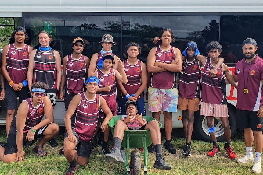15 indigenous students and teachers standing in front of a bus and their wheelbarrow 