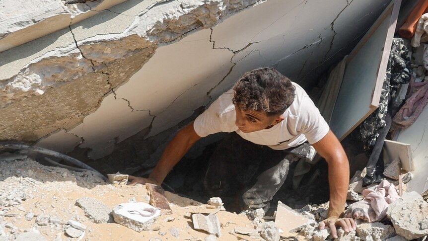 A man inspects as Palestinians search for casualties at the site of an Israeli strike on a house.