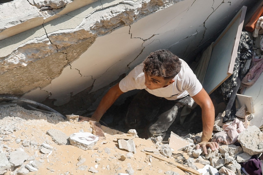 A man inspects as Palestinians search for casualties at the site of an Israeli strike on a house.